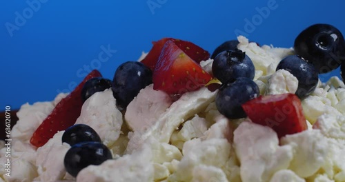 Extreme close up human hamd putting strawberries and blueberries on  cottage cheese rotate on a brown plate on a blue background.