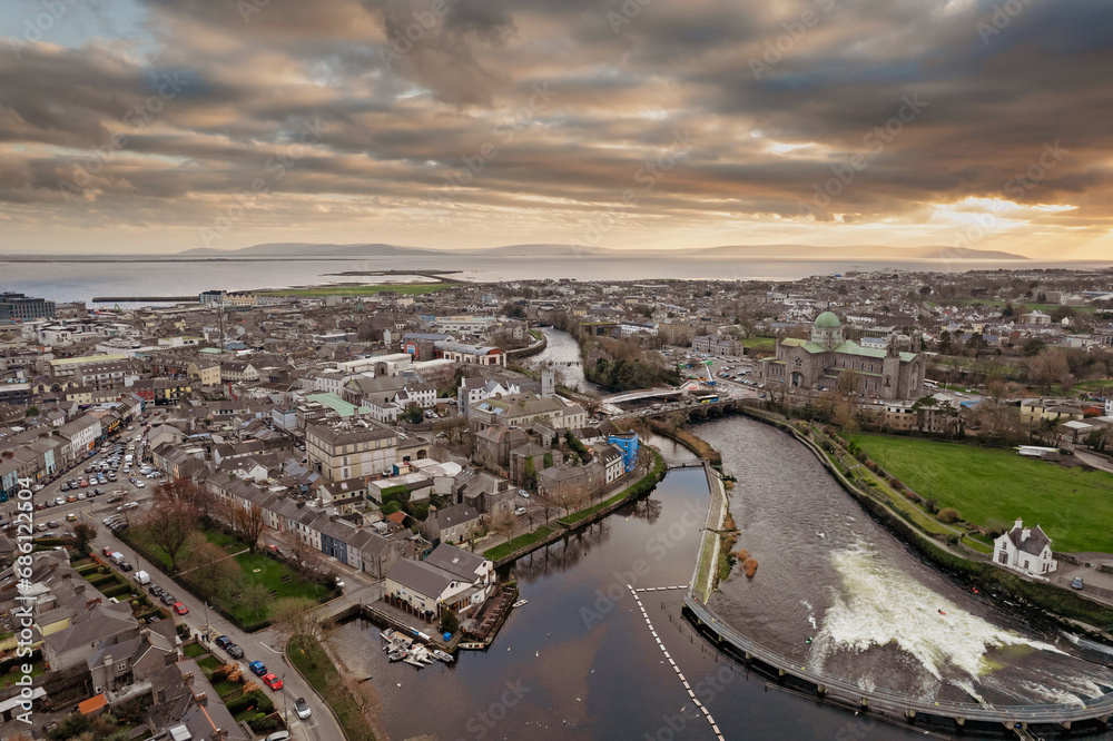 Aerial view on Salmon Weir in River Corrib, Galway city, Ireland. Dramatic cloudy sky. Cityscape scene. Water dam and bridge over the river. Galway Cathedral, popular tourist area.
