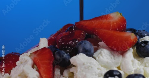 Extreme close up  cottage cheese with  strawberries and blueberries rotate on a brown plate on a blue background topping pouring on it