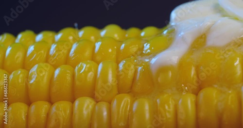 Extreme close up piece of butter melting on a cob of boiled delicious hot corn rotating  on a black background.