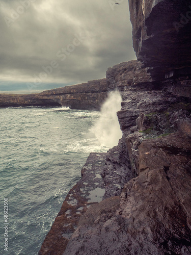 Rough stone coast and cliff of Aran Island, county Galway, Ireland. Nobody. Cloudy sky. Irish nature scene landscape. Dark and dramatic mood. Dún Aonghasa fort in the background.