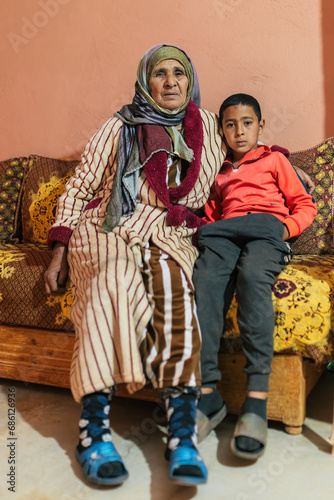 Cheerful Islamic grandmother and grandson sitting on sofa in living room
