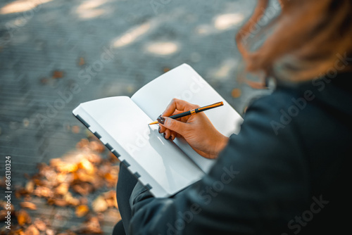 Young woman writing in a diary in an autumn park. Closeup image of a woman writing on a blank notebook. Woman working outdoors. photo