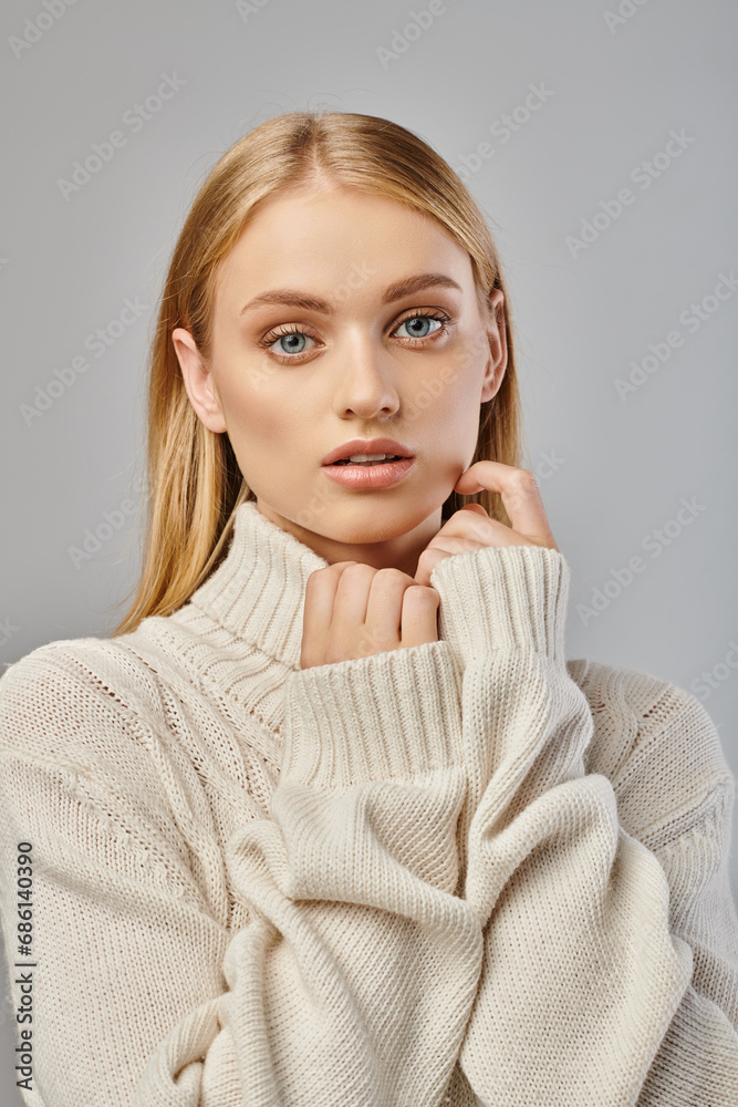 pensive woman with blonde hair and natural makeup in white winter sweater looking at camera on grey pensive woman with blonde hair and natural makeup in white winter sweater looking at camera on grey