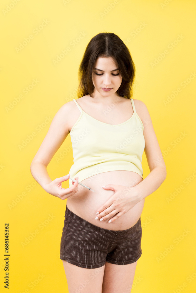 pregnant woman holding insulin syringe against her belly at colorful background with copy space. Diabetes concept pregnant woman holding insulin syringe against her belly at colorful background with copy space. Diabetes concept
