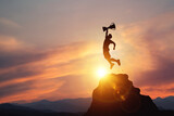 Silhouette of a businessman jumps holding a trophy on top mountain with light sunset. concept of a successful business or determination to lead the organization to success.