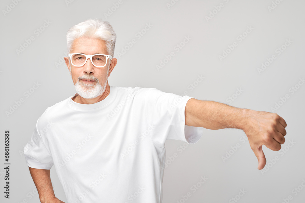 Portrait of elderly gray-haired man showing thumbs down isolated on white studio background. Dislike, wrong choice, negative evaluation concept Portrait of elderly gray-haired man showing thumbs down isolated on white studio background. Dislike, wrong choice, negative evaluation concept
