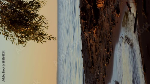 Meditative shot of the setting summer sun, calm waves on the sandy shore after kids played on sandy beach  vertical photo