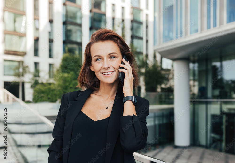 Portrait of a smiling middle-aged female in formal wear making a phone call while standing outdoors Portrait of a smiling middle-aged female in formal wear making a phone call while standing outdoors