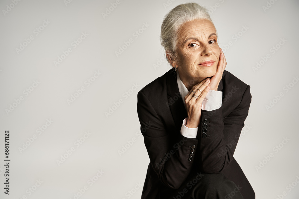 business portrait of mature businesswoman with grey hair posing in formal wear on grey background