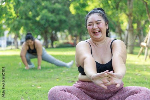 Asian female overweight in sportswear training exercise to lose weight on mat looking preview with laptop. woman plus size training online practice yoga in park. concept of healthy.