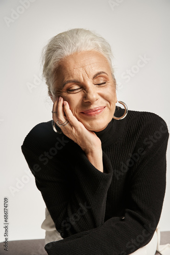 business portrait, pleased middle aged business woman with closed eyes posing in turtleneck on grey