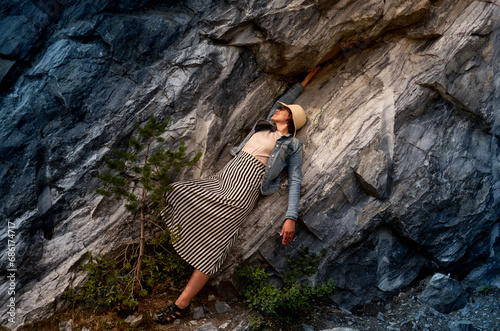 A female tourist in a straw hat and denim jacket poses against the background of a natural marble wall