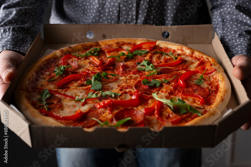 Caucasian male hands hold large open carton box with pepperoni pizza with arugula front view photo