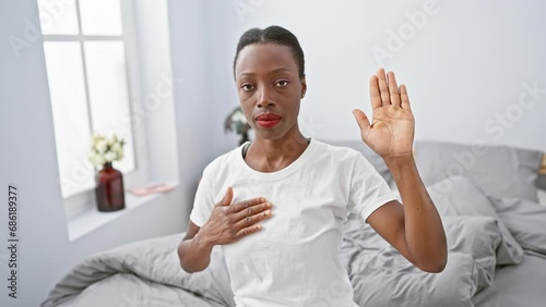 Solemn oath in the comfort of home, beautiful african american woman lies on the bed, hand over heart, pledging loyalty with a proud and sincere swear in a relaxing bedroom atmosphere.