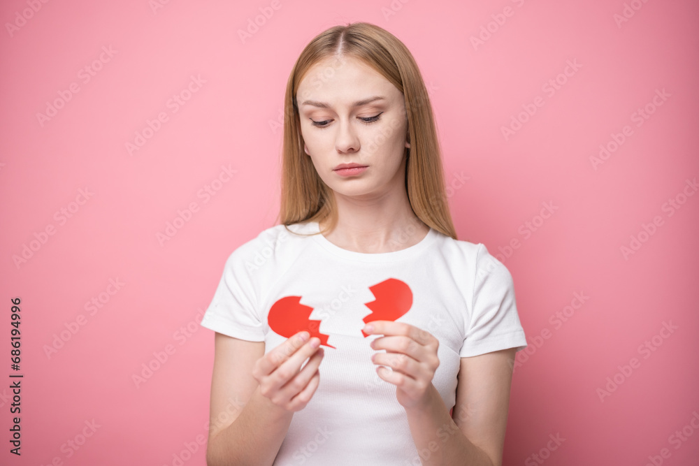 Beautiful girl on pink background with red broken heart. Concept of breakup, quarrel, divorce, unrequited love. Beautiful girl on pink background with red broken heart. Concept of breakup, quarrel, divorce, unrequited love.