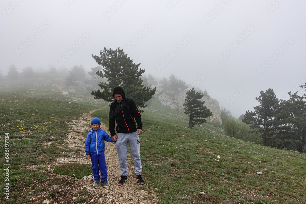 A picturesque mountain landscape in the clouds on Ai-Petri mountain in the Crimea. A man with a boy on the background of a high-altitude landscape with trees in the clouds.