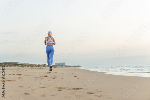 sportive woman running along beautiful sandy beach enjoying active summer near the sea © PopOff