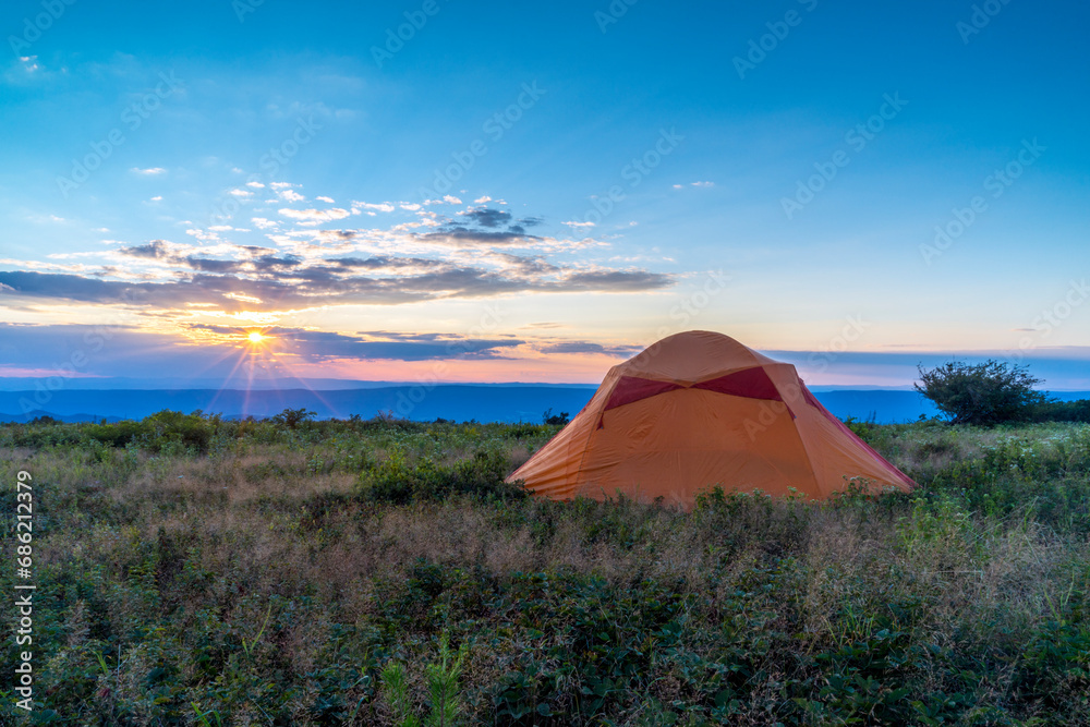 Sunrays warmly shine over a peaceful campsite at the edge of a mountain meadow.