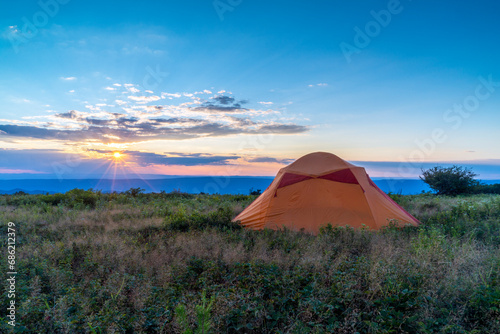 Sunrays warmly shine over a peaceful campsite at the edge of a mountain meadow.
