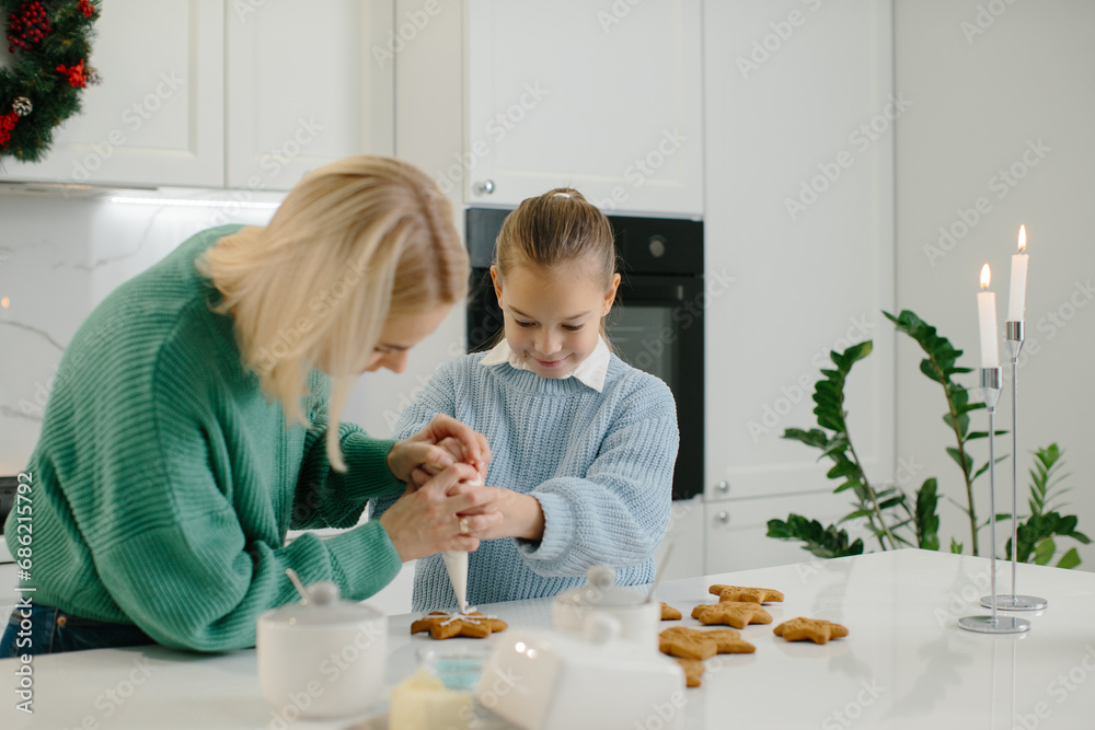 Mother and daughter decorate Christmas cookies in the kitchen.