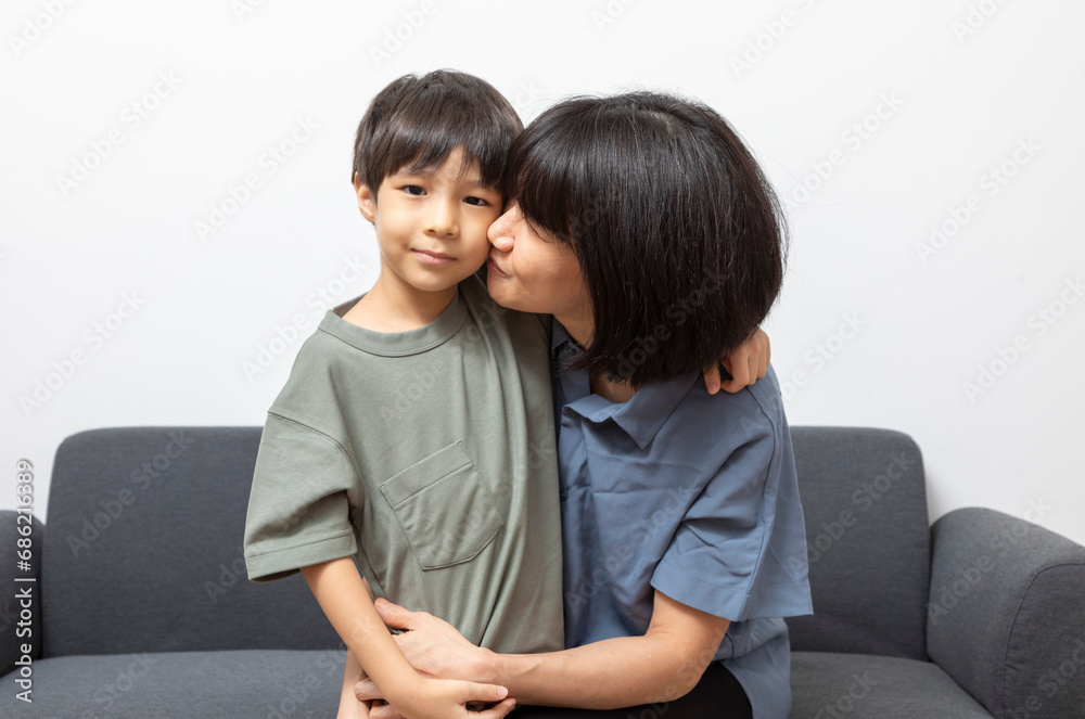 Portrait of happy Asian woman and her little son hugging and sitting on sofa at home. Portrait of happy Asian woman and her little son hugging and sitting on sofa at home.