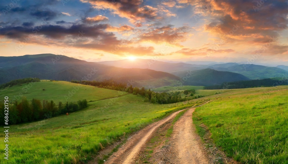 beautiful summer mountain rural landscape panorama of summer green field with dirt road and sunset cloudy sky