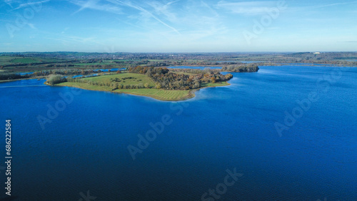 Aerial view 4k wide angle of fields and Rutland water, England, cloudy skies and green patches of forest.