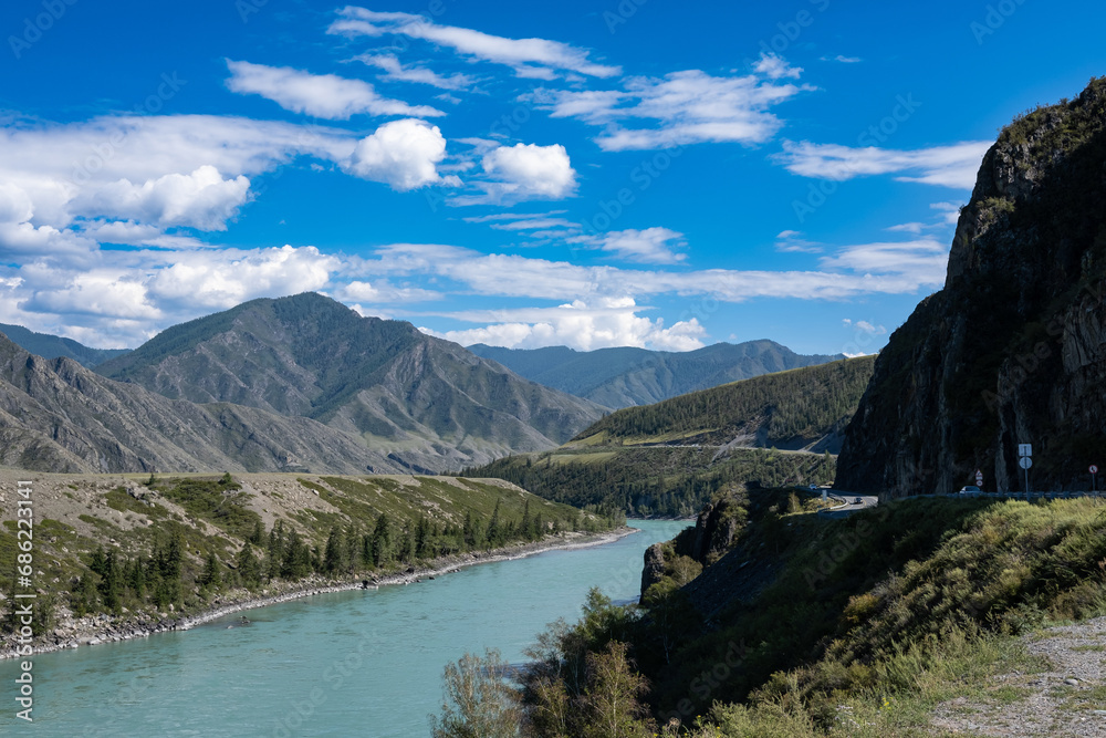 Beautiful mountain landscape with a river on a bright sunny day. White clouds in a blue sky. The Katun River in the Altai Republic, part of the Chui tract