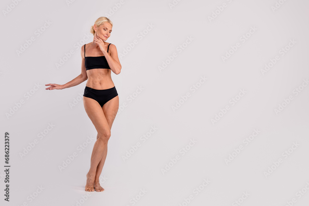 Full body photo of slim charming successful sportswoman mature posing strong muscles black under clothes isolated on gray color background