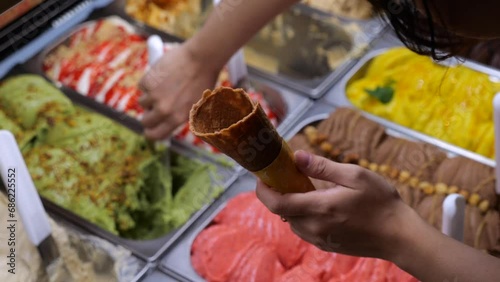 Seller puts sweet scoop of ice cream from tray into crispy cone. Range of gelato ice cream is amazing in its diversity. Ice cream is favorite dessert of adults and children.