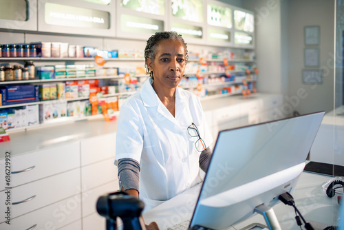 Senior female pharmacist working on computer at drugstore photo