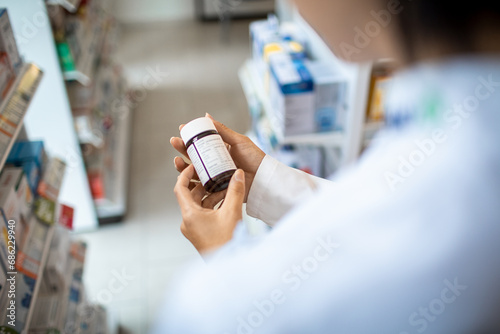 Pharmacist holding medication bottle reading label in pharmacy drugstore photo