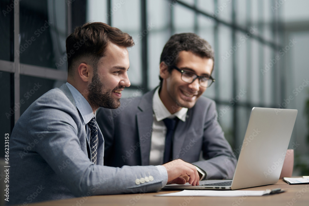 Fototapeta premium Two young businessmen sitting at workplace and working together in office