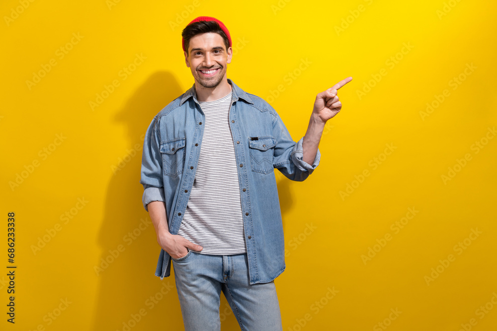 Photo of good mood positive guy wear denim jacket showing finger empty space isolated yellow color background Photo of good mood positive guy wear denim jacket showing finger empty space isolated yellow color background