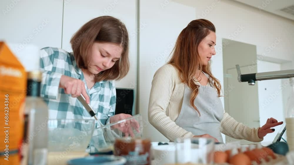 Serious mom and daughter watching recipe on tablet and cooking in kitchen Serious mom and daughter watching recipe on tablet and cooking in kitchen