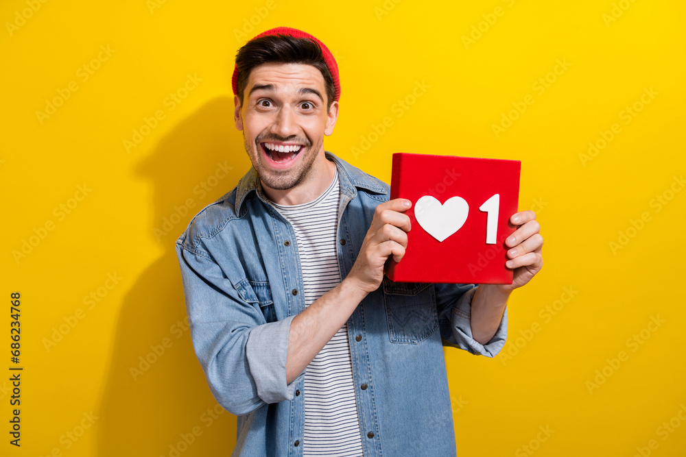 Photo of excited funky guy wear denim jacket rising positive heart like card isolated yellow color background Photo of excited funky guy wear denim jacket rising positive heart like card isolated yellow color background