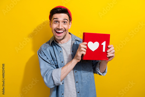 Photo of excited funky guy wear denim jacket rising positive heart like card isolated yellow color background © deagreez