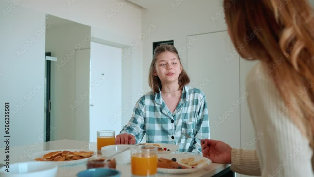 Positive mom and daughter eating berry pancakes and talking in the kitchen Positive mom and daughter eating berry pancakes and talking in the kitchen
