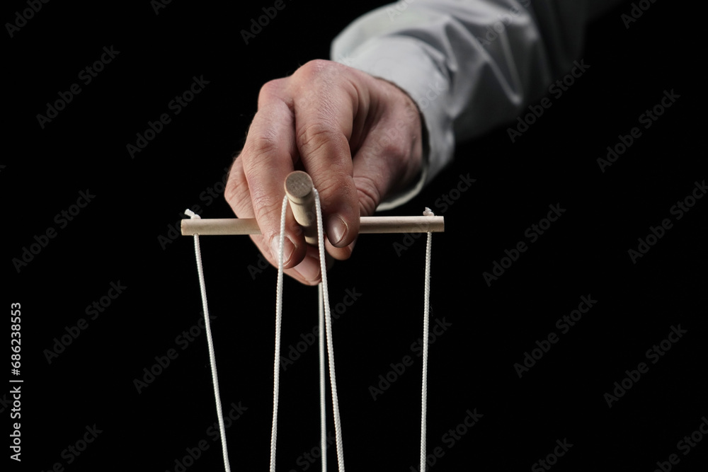 In a close up shot against a black background. A mans hand that holds a device with a puppeteers string. Demonstrates a dominant man, a businessman, an executive. Theatrical performance, manipulation In a close up shot against a black background. A mans hand that holds a device with a puppeteers string. Demonstrates a dominant man, a businessman, an executive. Theatrical performance, manipulation
