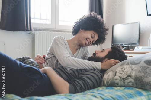 Obraz na plátně Young multiethnic couple hugging lying bed at home cuddling