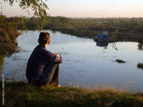 Girl sitting on a hill against the backdrop of a lake at sunset