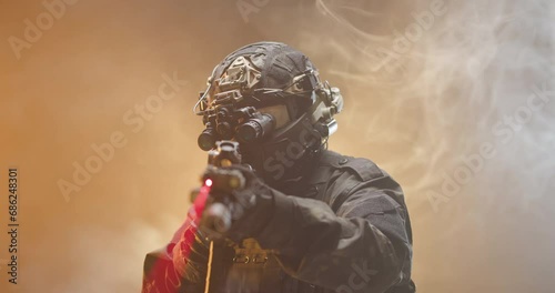 Soldier fully equipped with tactical gear and protection aiming his rifle at enemy with orange smoke in the background. photo