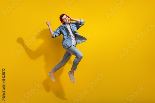 Full length photo of impressed lucky guy wear denim jacket jumping enjoying songs walking empty space isolated yellow color background © deagreez