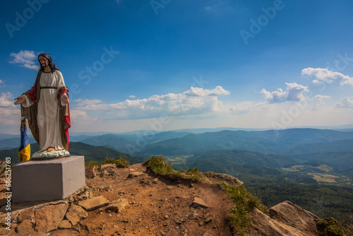 Jesus statue on top of a mountain. Beautiful view of the Ukrainian Carpathians to the mountains and valleys. Rain clouds in the mountains. Yellow and green grass, and the top of the mountain. photo