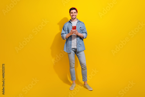 Full length photo of cheerful cool guy wear denim jacket chatting instagram twitter telegram facebook isolated yellow color background © deagreez