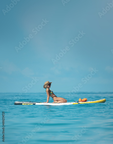 sexy girl in a swimsuit on a sup board lies resting on a board under the bright sun on the background of the sea , Stand up paddleboarding © rotozey
