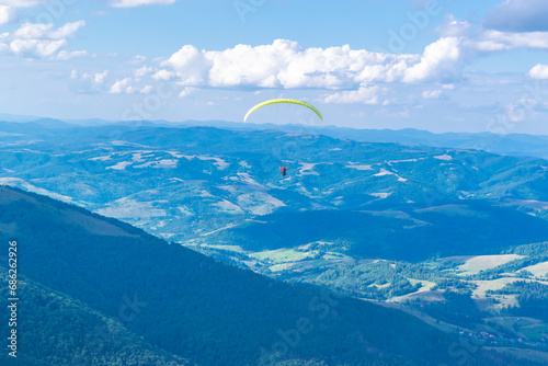 Paragliding flight with an instructor. Silhouette of paraglider against background of a beautiful landscape of blue cloudy sky and green mountains.