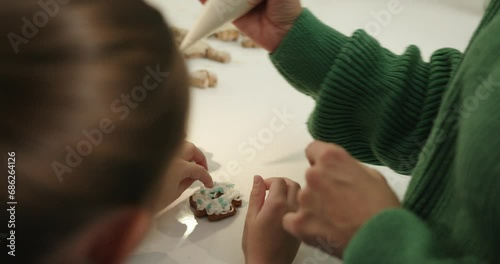 Close-up, Mother and daughter prepare Christmas gingerbread cookies and decorate them with icing and colorful sprinkle. photo