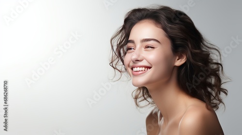 A young girl, who is beautiful and clean-shaven, laughs and smiles joyfully while standing over a white background.